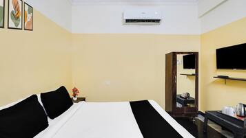 Habitación de hotel con una cama, un televisor de pantalla plana montado en la pared, una mesita con un hervidor y un espejo.