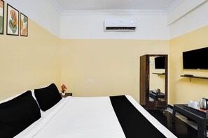 Habitación de hotel con una cama, un televisor de pantalla plana montado en la pared, una mesita con un hervidor y un espejo.