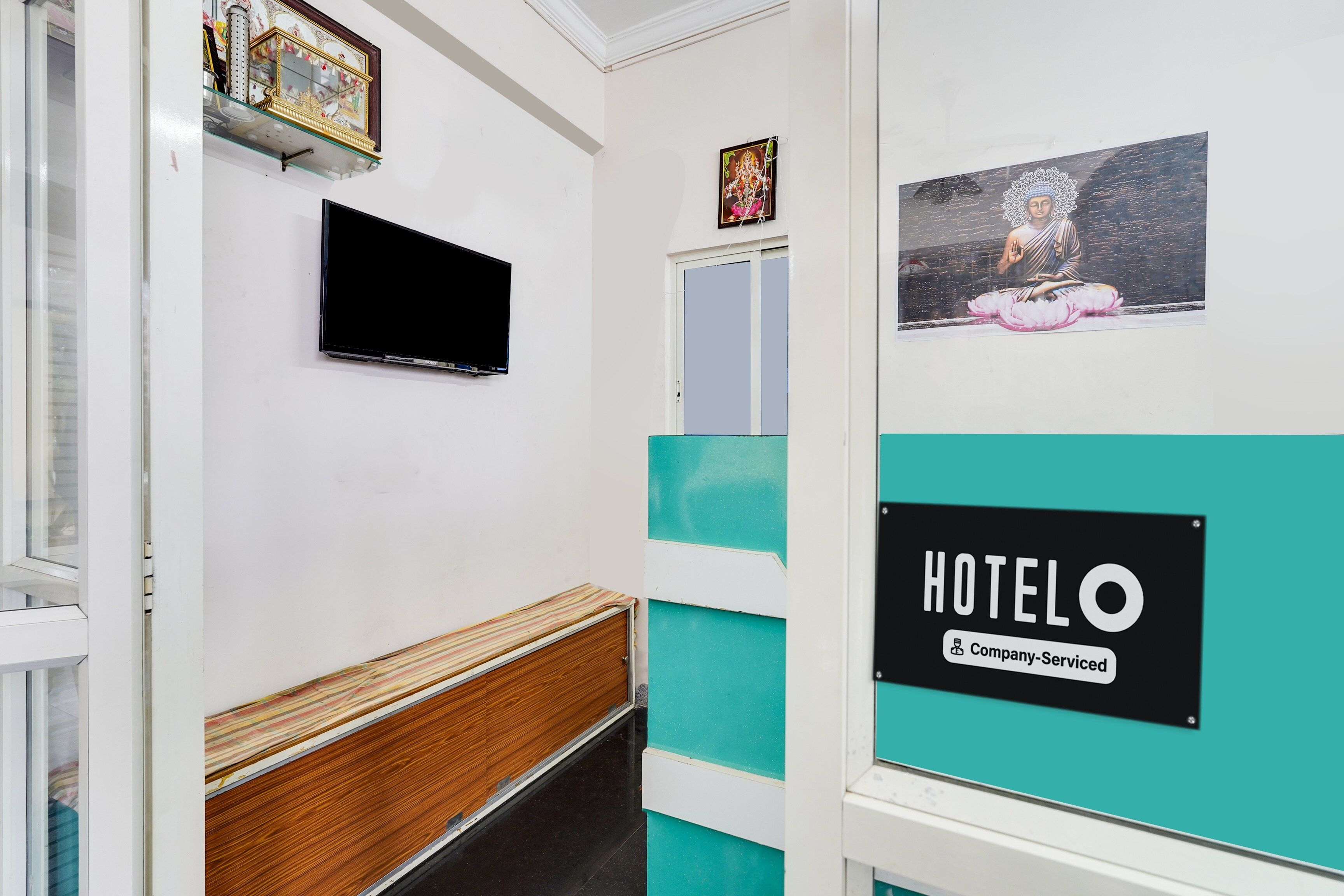 A hotel corridor with a wooden bench, a flat-screen TV mounted on the wall, and a sign indicating the hotel is company-serviced.