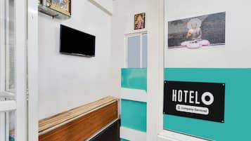 Un pasillo de hotel con un banco de madera, un televisor de pantalla plana montado en la pared y un cartel que indica que el servicio es proporcionado por la empresa.