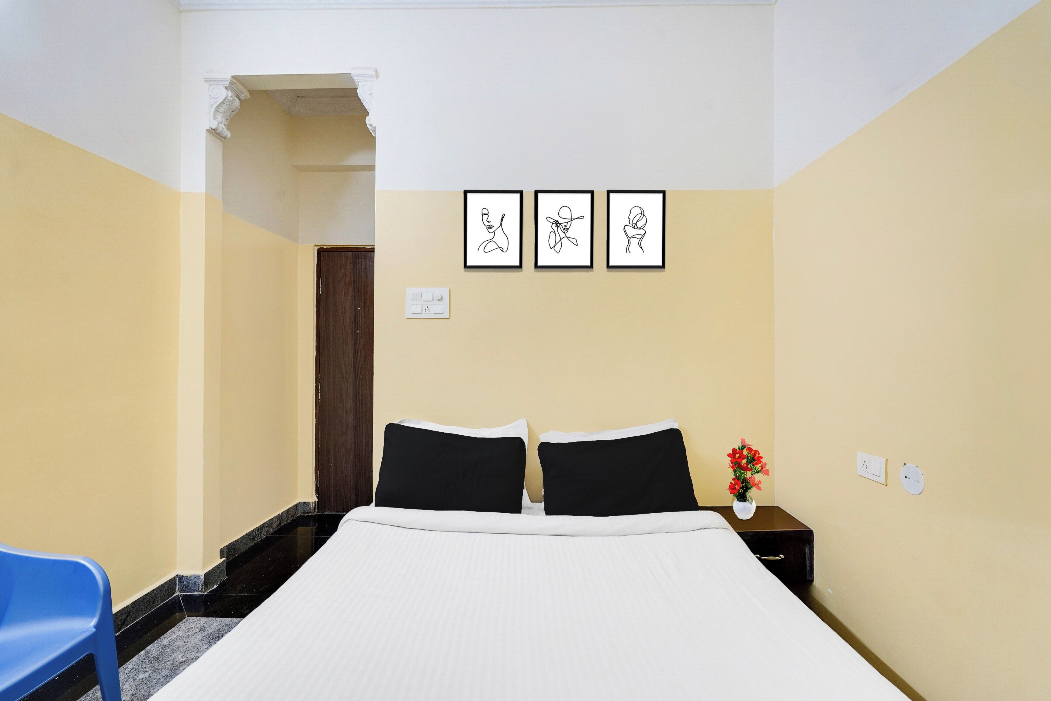 Una habitación de hotel con una cama, dos mesitas de noche, una silla azul y una puerta que da a otra habitación.