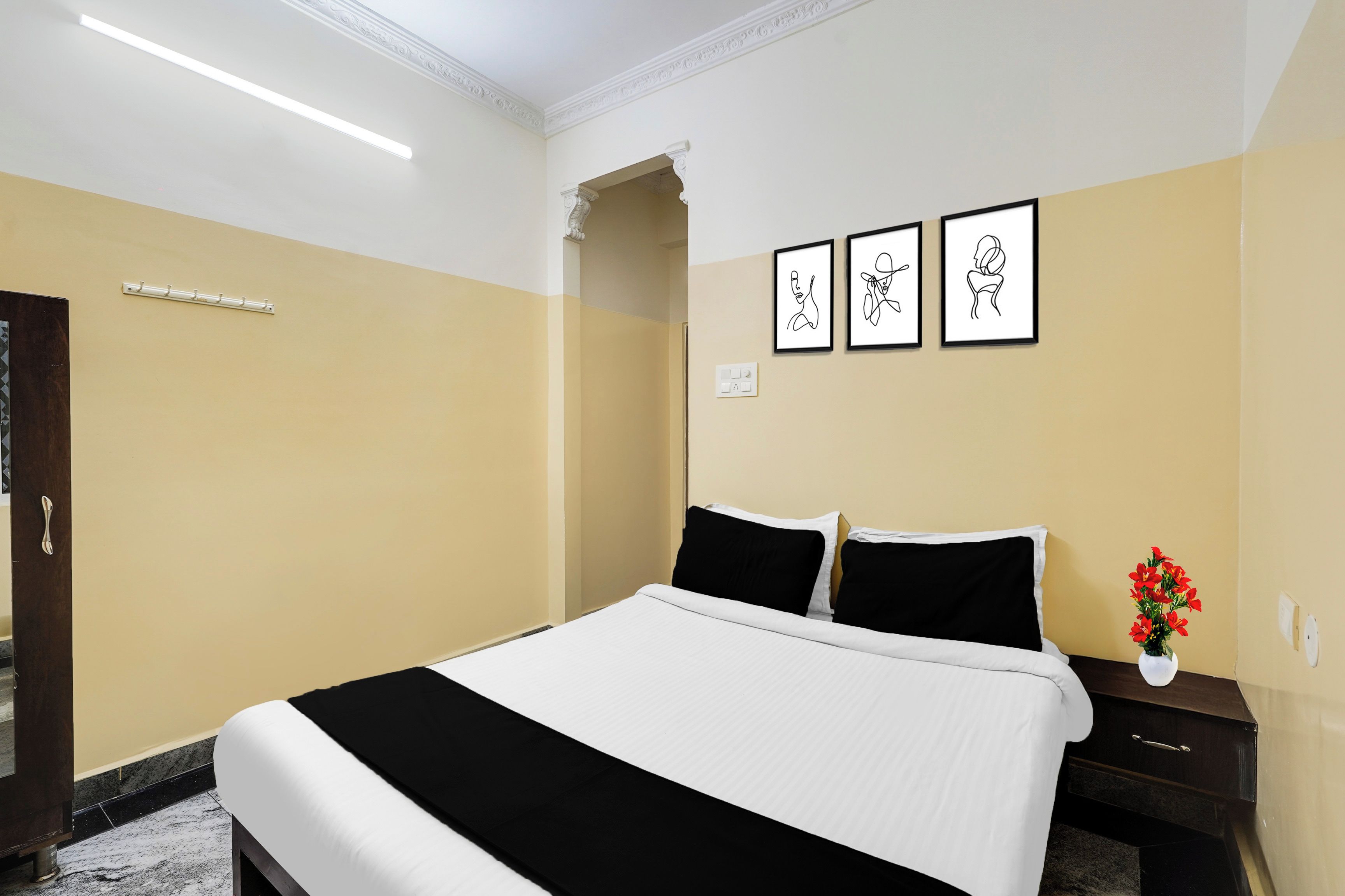 A hotel room with a bed, a nightstand, a vase with flowers, and three framed artworks on the wall.