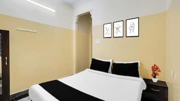 Habitación de hotel con una cama, una mesita de noche, un jarrón con flores y tres cuadros en la pared.