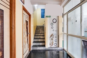 A hallway with a wooden door on the left, a staircase leading to a room, and a door with a fire exit sign above it.