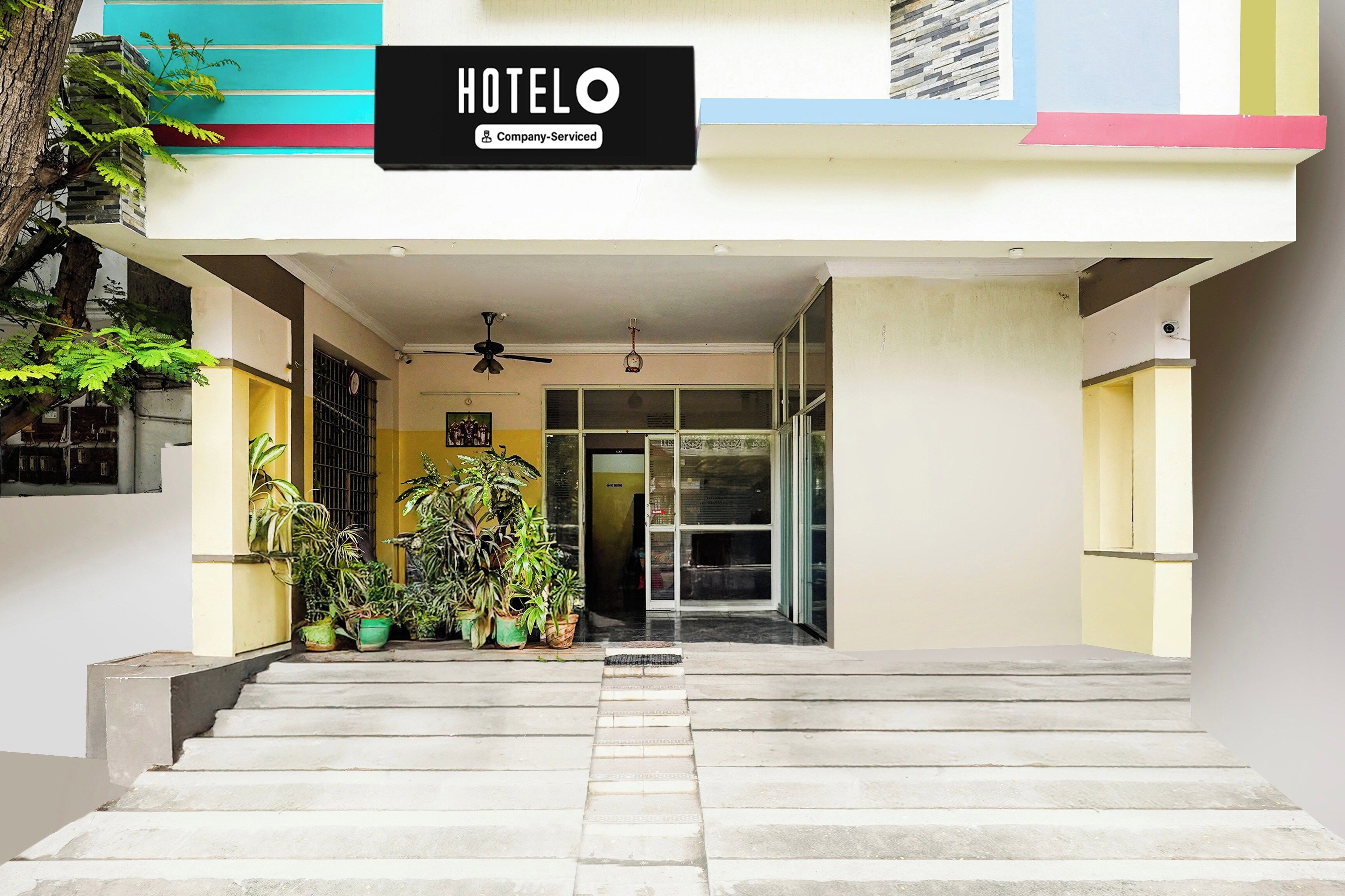 Entrada de un hotel con un letrero que dice 'HOTEL Company Serviced', una escalera que sube y plantas en macetas a la entrada.