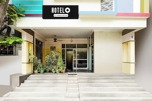 Entrada de un hotel con un letrero que dice 'HOTEL Company Serviced', una escalera que sube y plantas en macetas a la entrada.
