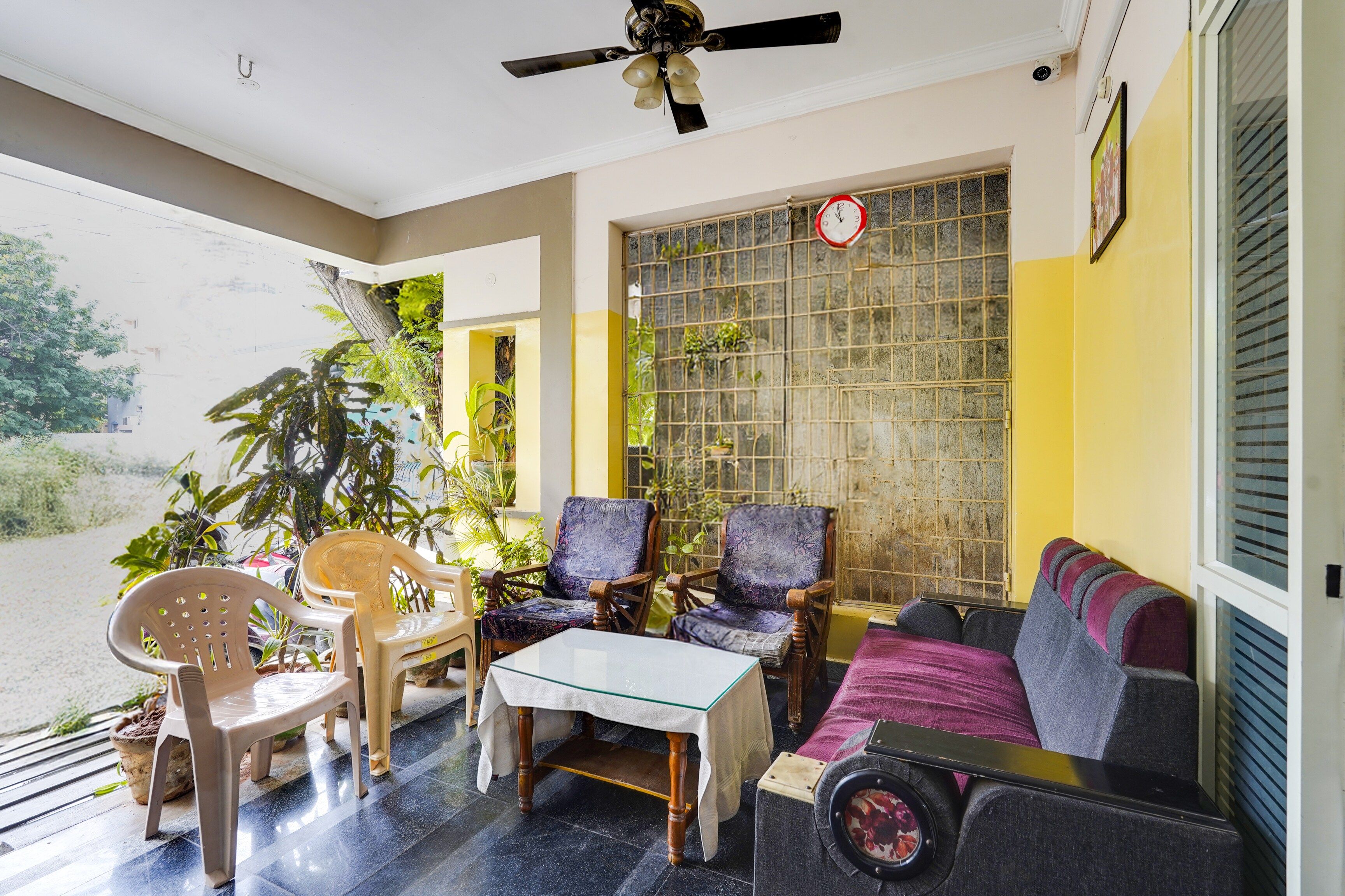 A room with a ceiling fan, a table, two chairs, a sofa, and a window with a metal grid.