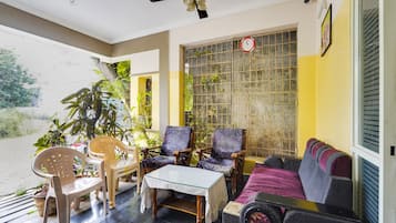 Una habitación con ventilador de techo, una mesa, dos sillas, un sofá y una ventana con celosía de metal.