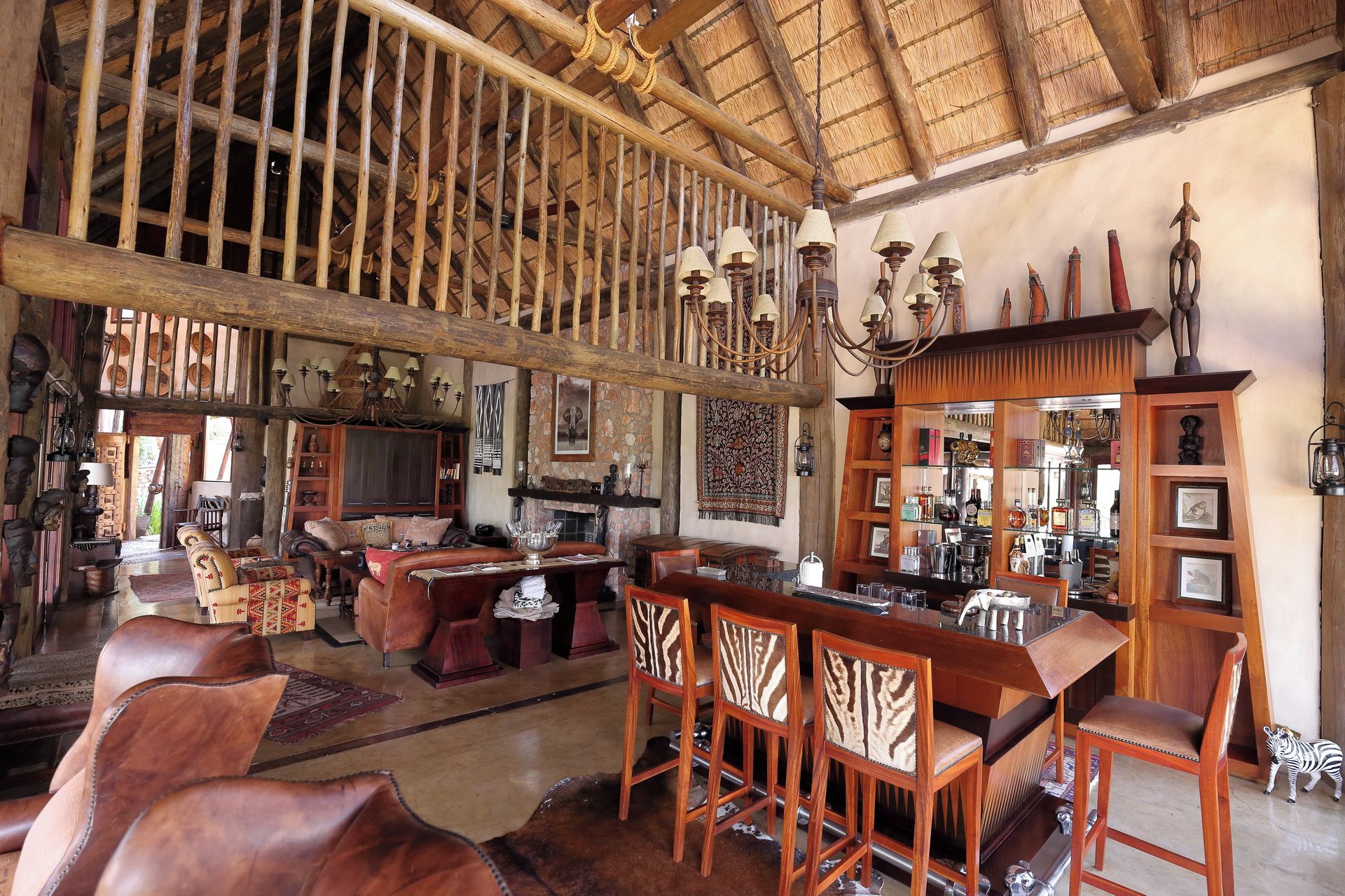 Un intérieur rustique avec un plafond haut, des poutres en bois, un coin bar avec des tabourets et divers éléments décoratifs.