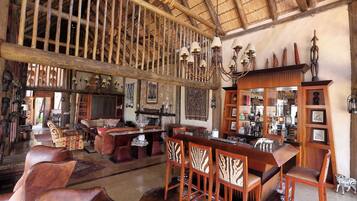 Un intérieur rustique avec un plafond haut, des poutres en bois, un coin bar avec des tabourets et divers éléments décoratifs.