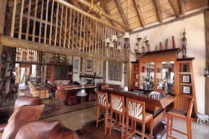Un intérieur rustique avec un plafond haut, des poutres en bois, un coin bar avec des tabourets et divers éléments décoratifs.