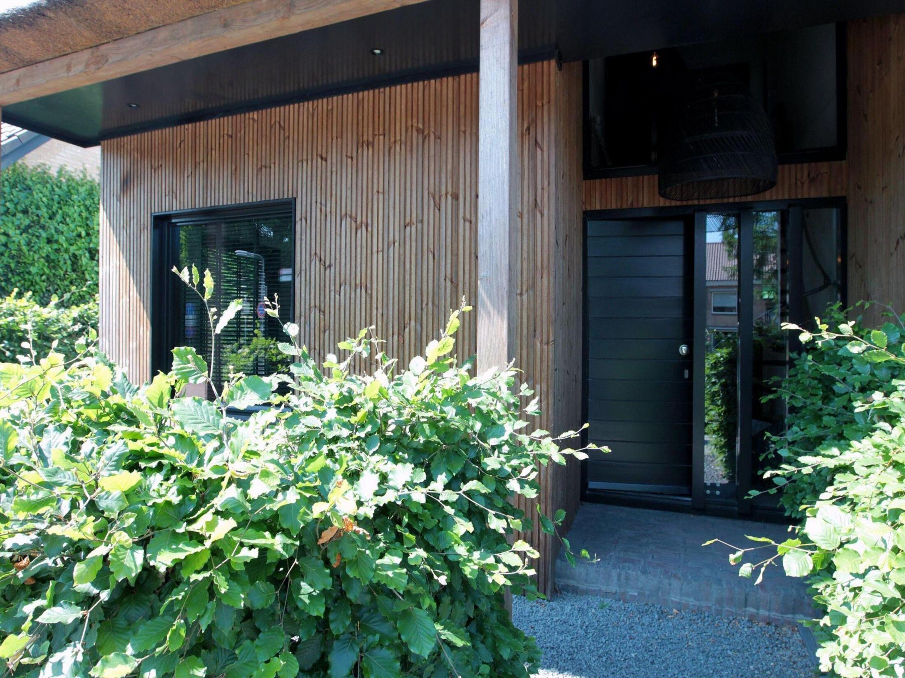 Un bâtiment moderne avec une façade en bois, une entrée dotée d’une porte en verre et un espace extérieur aménagé avec des sièges.