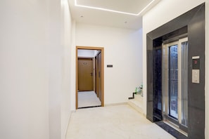 A modern hallway with a marble floor, a wooden door leading to room 201, and a glass elevator with a digital display. - Super Collection O Ujjain Central (Ujjain)