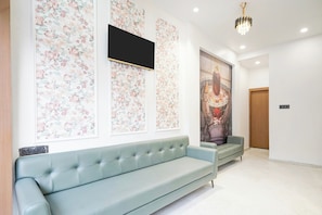 A modern interior with a light blue sofa, floral wallpaper, a large framed artwork, and a chandelier. - Super Collection O Ujjain Central (Ujjain)