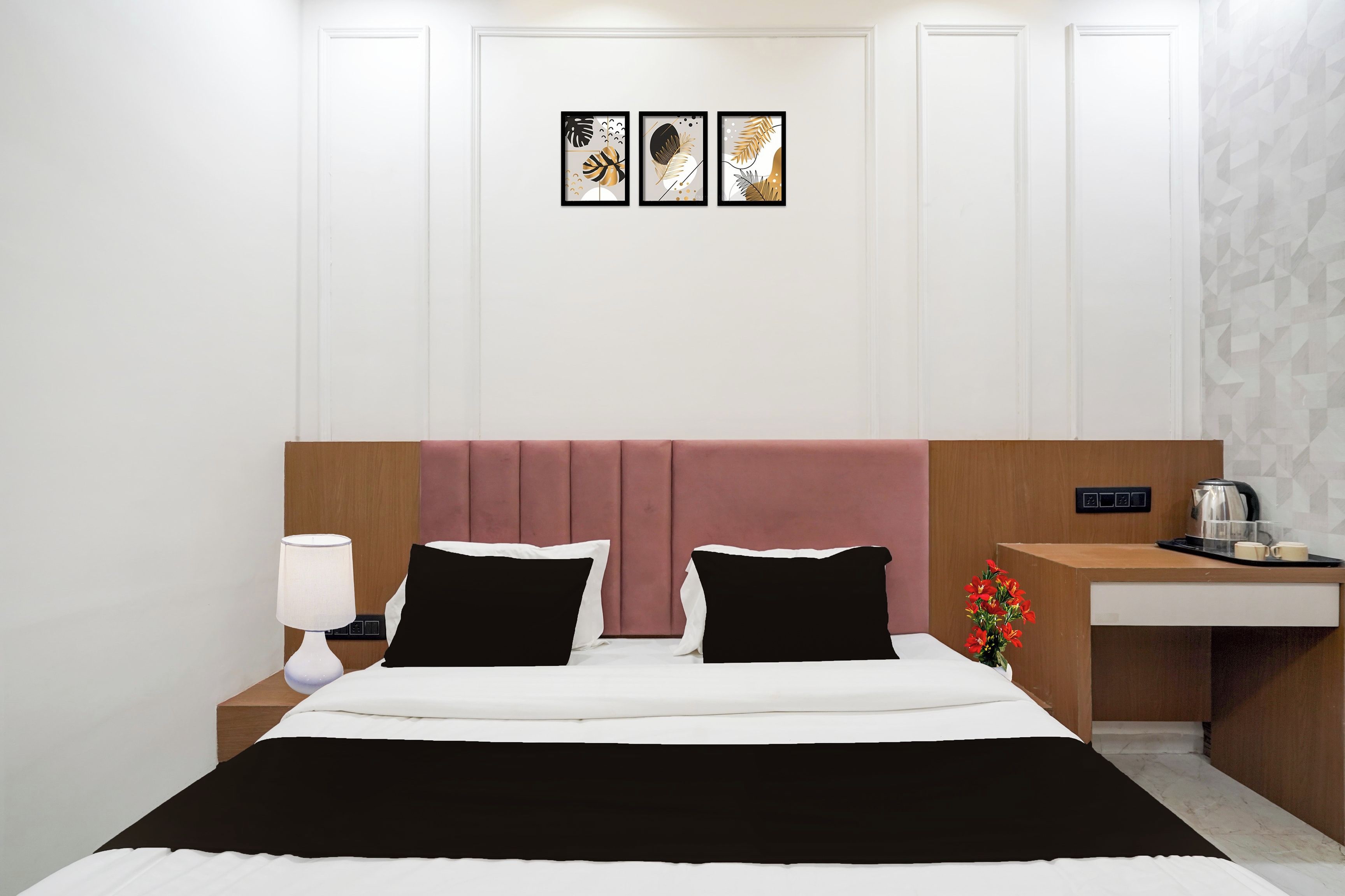 A hotel room with a bed, bedside table, lamp, and a small desk with a kettle.