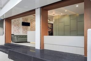 A reception area with a grey sofa, a flat-screen TV mounted on the wall, and a decorative floral wallpaper. - Super Collection O Ujjain Central (Ujjain)