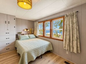 Un dormitorio con cama, armario, ventana con cortinas y lámpara colgante.