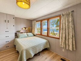 Un dormitorio con cama, armario, ventana con cortinas y lámpara colgante.