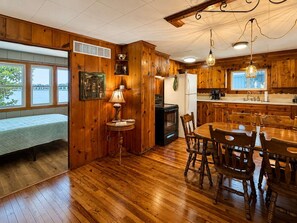Un interior de madera con una mesa de comedor, sillas, estufa y un banco junto a una ventana.