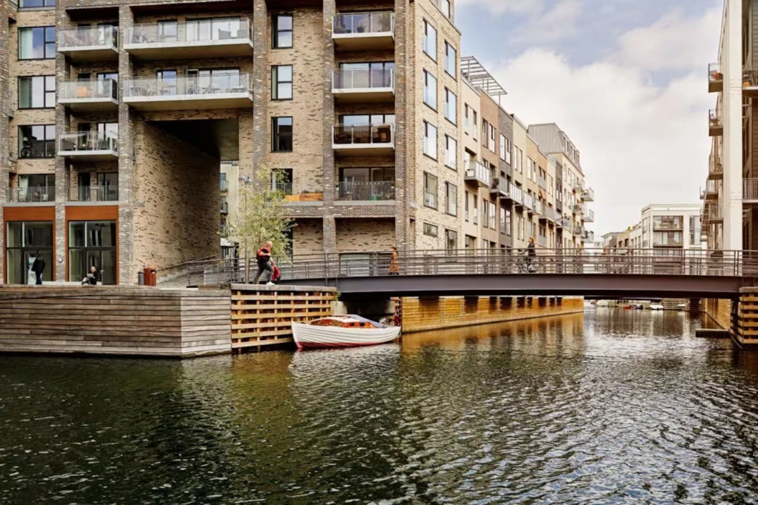 A canal with a boat, a pedestrian bridge, and multi-story buildings with balconies.