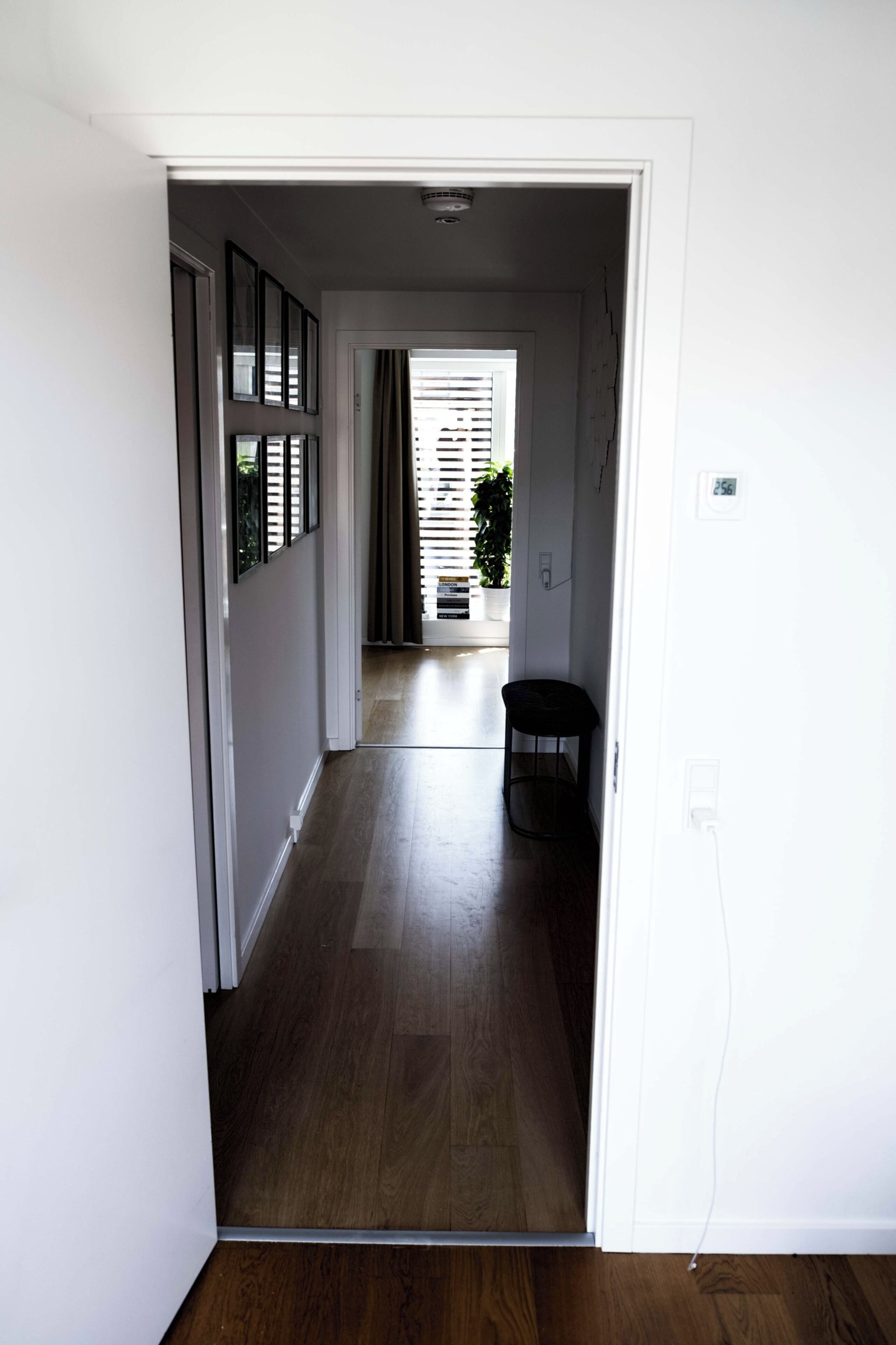 A hallway with a wooden floor, a door leading to another room, and a power outlet on the wall.