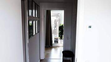 A hallway with a wooden floor, a door leading to another room, and a power outlet on the wall.