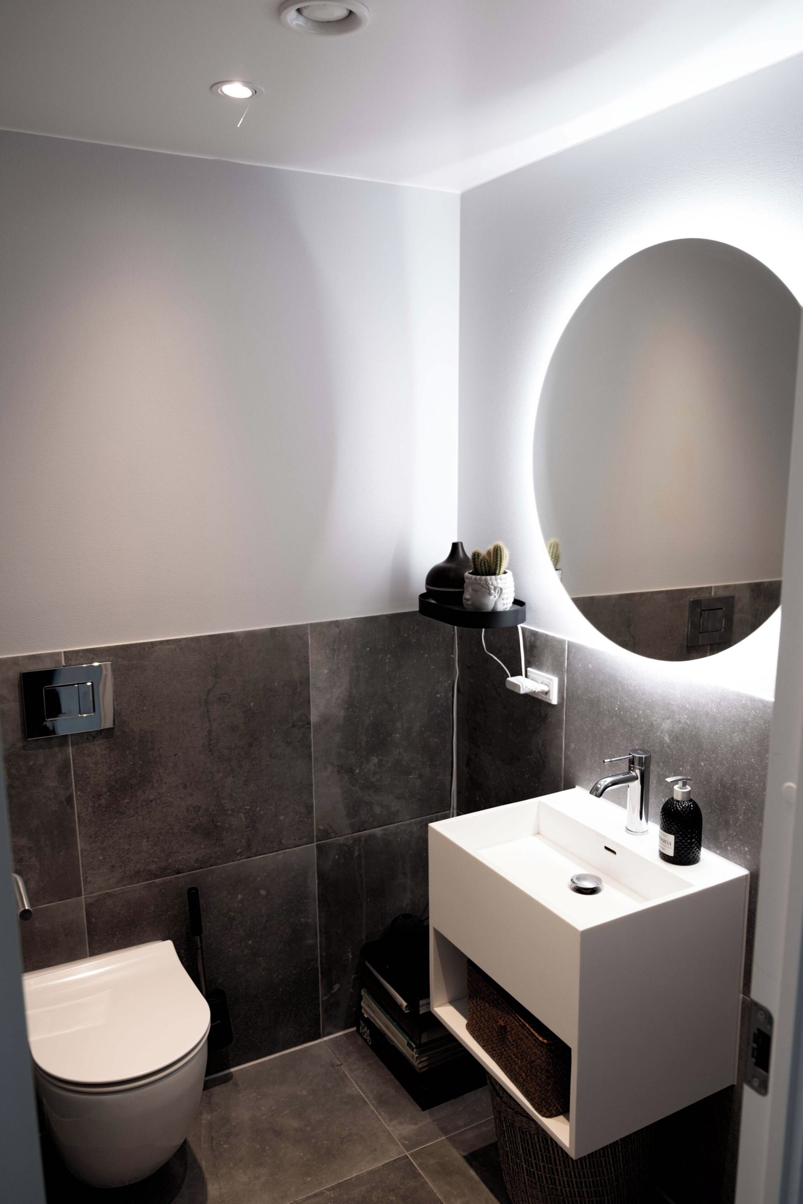Et moderne badeværelse med en hvid vask, et rundt spejl og et toilet.