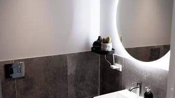 Et moderne badeværelse med en hvid vask, et rundt spejl og et toilet.