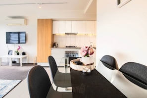 A modern kitchen with white cabinets, a wooden panel, and a dining area with a glass table and black chairs. - Well Equipped 2BDR Apt in Southbank with Parking (Southbank)