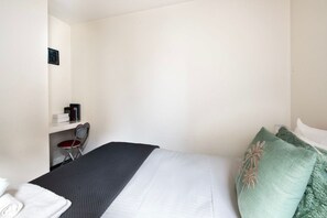 Une chambre d’hôtel avec un lit, une chaise, un bureau et une petite étagère.