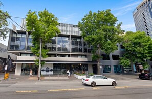 A modern building with large windows and a flat roof, surrounded by trees and a street with cars. - Well Equipped 2BDR Apt in Southbank with Parking (Southbank)