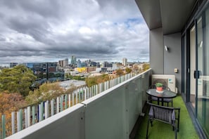 A balcony with a view of a city skyline, a table with chairs, and a potted plant. - Well Equipped 2BDR Apt in Southbank with Parking (Southbank)