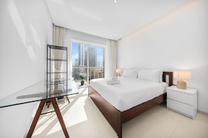 A modern hotel room with a large bed, a glass desk, a nightstand, and a view of high-rise buildings. - StayShort - Chic 1 Bedroom Haven Perfect for 2 in Dubai Marina! (Dubai Marina)