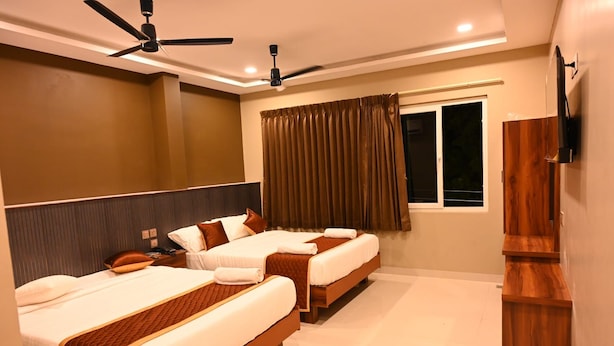 Quarto de hotel com duas camas, televisão na parede e janela com cortinas.