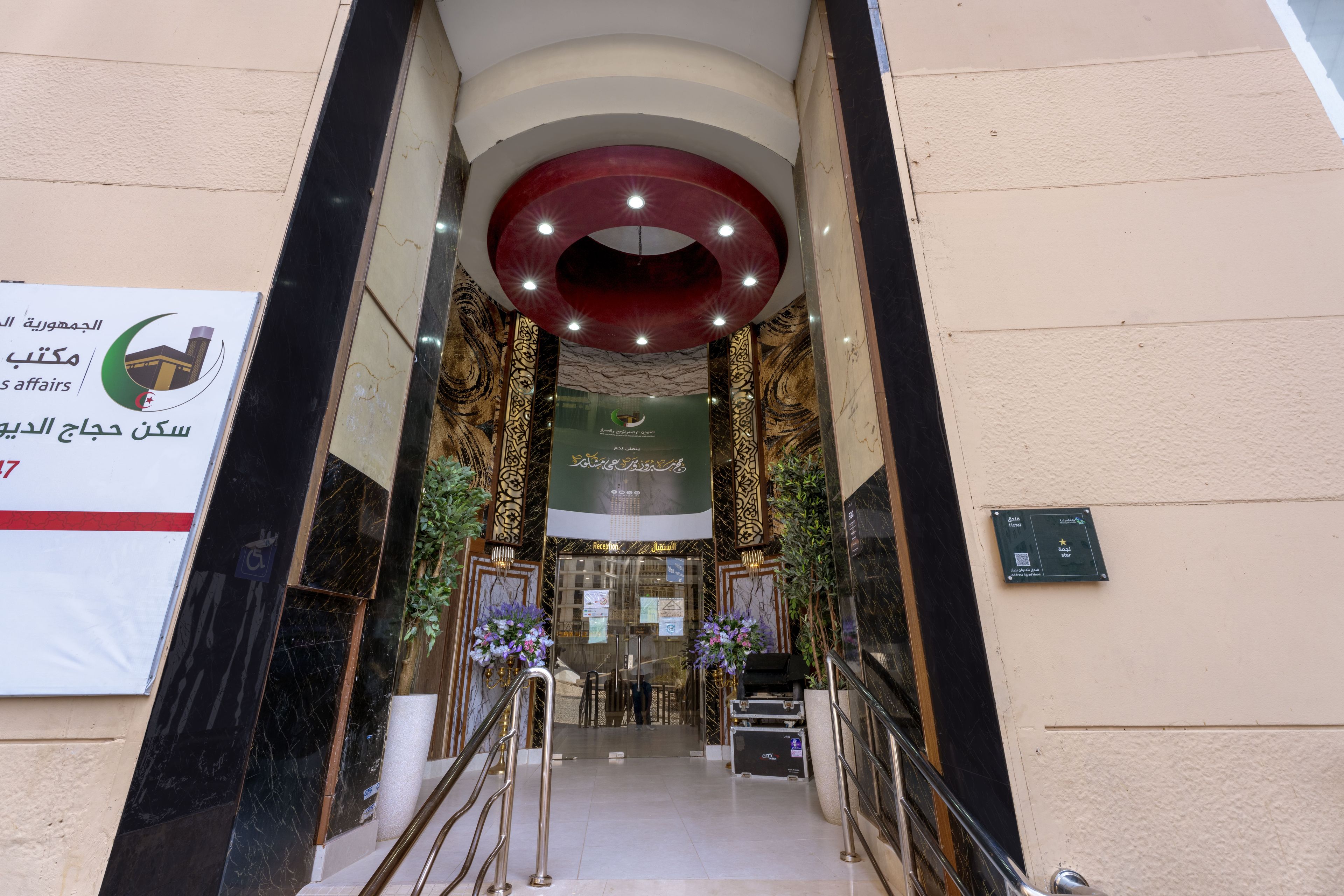 A hotel entrance with a reception desk, a staircase, and a sign indicating the hotel's name.