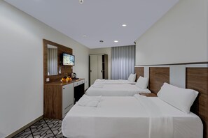 Una habitación de hotel con dos camas, un escritorio con televisor y la puerta del baño.
