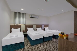 Una habitación de hotel con tres camas, un escritorio pequeño y una cesta de frutas.