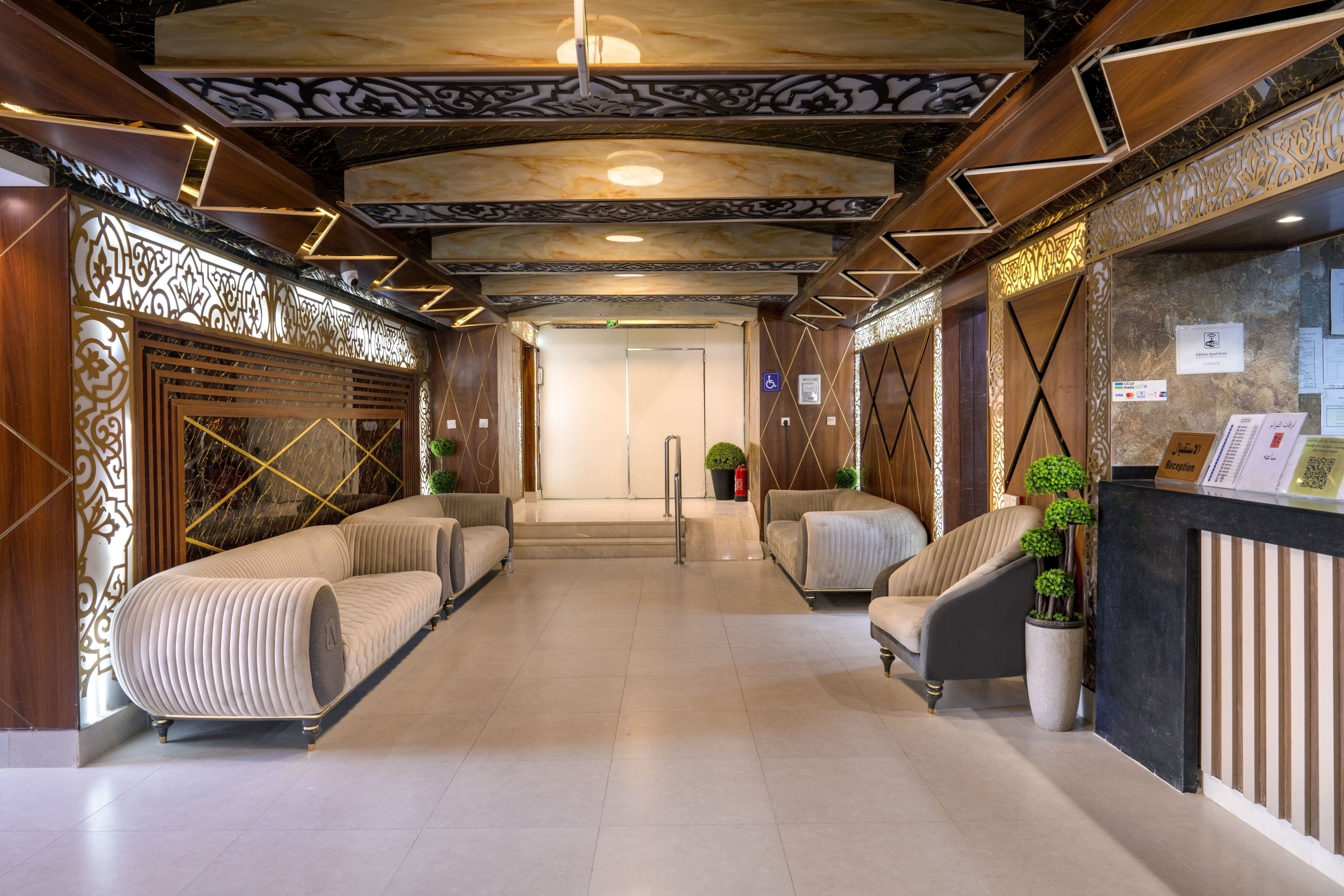 Een hotel receptie met een modern ontwerp, met een receptiebalie, een zithoek met banken en een decoratief plafond.