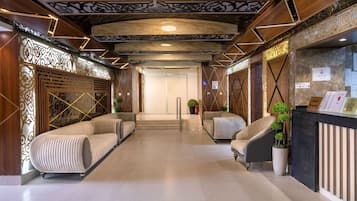 Een hotel receptie met een modern ontwerp, met een receptiebalie, een zithoek met banken en een decoratief plafond.