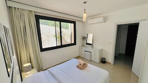 Ett hotellrum med en säng, ett nattduksbord, en lampa, en byrå och ett fönster med gardiner.