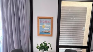 En matplats med ett runt bord i glas, två grå stoppade stolar, en krukväxt och en inramad tavla på väggen.