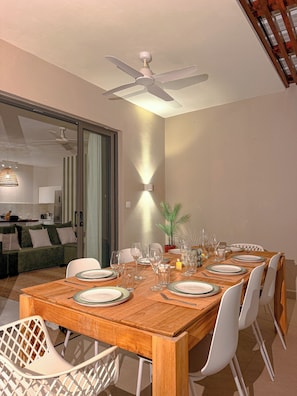 A dining area with a wooden table set for six, white chairs, and a ceiling fan above. - The Pearl Villa - With private pool (Petit Raffray)
