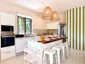 A modern kitchen with white cabinetry, a central island, and a striped wall. - The Pearl Villa - With private pool (Petit Raffray)