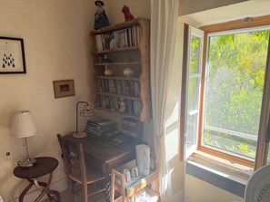 A cozy room with a wooden desk, bookshelves, a lamp, and a window with a view of trees. - Bed and Breakfast 'Chambres Les Chats' with Mountain View, Shared Garden and Wi-Fi (Châteaudouble)