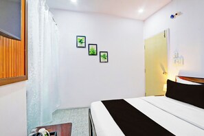 Habitación de hotel con cama, puerta, lámpara de pared y tres cuadros enmarcados.