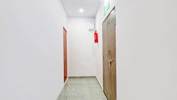 A corridor with a fire extinguisher mounted on the wall, a door with a handle, and a ceiling light.