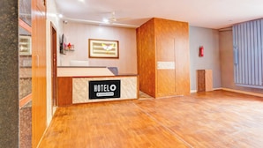 Een hotel receptie met een houten balie, een ingelijst beeld van een duif, een brandblusser en een plafondventilator.