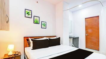 Quarto de hotel com cama, mesa de cabeceira com abajur e telefone, porta de madeira e três quadros de plantas na parede.