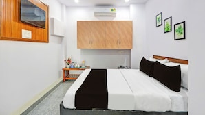 Een hotelkamer met een bed, een aan de muur bevestigde televisie, een houten kast, een klein tafeltje met een kan en ingekaderde foto's.