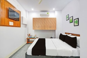 A hotel room with a bed, a TV mounted on the wall, a wooden cabinet, a small table with a pitcher, and framed pictures on the wall. - Hotel O Karmanghat Near TKR khaman (Hyderabad)